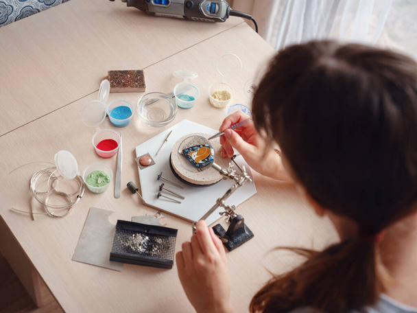 ライフスタイルの概念は、あなたの人生を再発明するために自宅から仕事-ジュエリーデザイナーの職場。女性はジュエリーを作る。グルジアのミナンカリエナメル製造技術。宝石商はワークショップでアクセサリーを作る. - 写真・画像