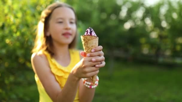 Милая девушка с брекетами едят итальянское мороженое конус улыбаясь во время отдыха в парке в летний день, ребенок наслаждается мороженым на открытом воздухе, счастливые праздники, лето - Кадры, видео