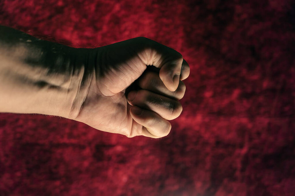 Man's fist. Hand of a mature man against a dark red background. Close-up. Selective focus. Defocus, noise, grain effect. - Foto, Imagen