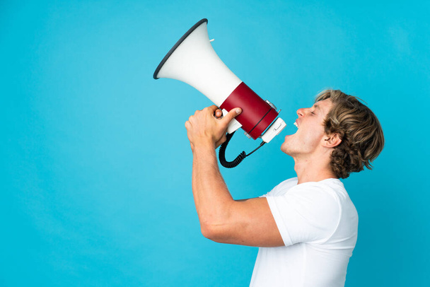 English man over isolated blue background shouting through a megaphone to announce something in lateral position - Photo, image