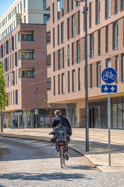 Odense, Dänemark - 23. Mai 2022: Mädchen oder Frau auf einem neuen Radweg oder einer neuen Straße zwischen modernen Gebäuden und Büros im Zentrum von Odense, Dänemark im Frühling oder Sommer, senkrecht - Foto, Bild