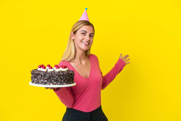 Blondi Uruguayn tyttö tilalla syntymäpäivä kakku eristetty keltaisella taustalla ulottuu kädet sivulle kutsuvan tulla - Valokuva, kuva