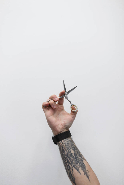 Un hombre guay con un tatuaje en el brazo sostiene un par de tijeras. El tipo es un peluquero profesional - Foto, imagen