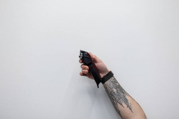 Mężczyzna z tatuażem trzyma spinacz na białym tle. Profesjonalny męski fryzjer. Redukcja wartości, koncepcja - Zdjęcie, obraz