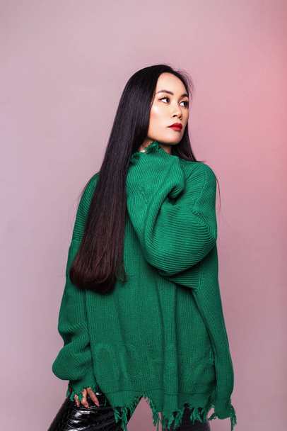 Glamorous beautiful Asian girl in a fashionable green knitted sweater poses in the studio with pink light - Fotografie, Obrázek