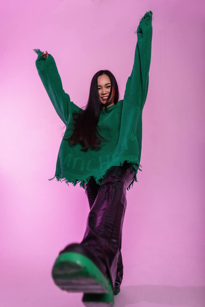 Дивна азійська модель в модному одязі з зеленим светром в модних шкіряних штанях і туфлях емоційно поставлена в студії - Фото, зображення