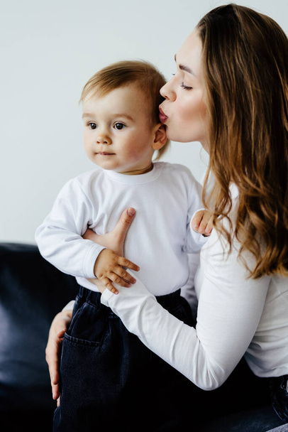 Szczęśliwy synek przytulający śmiejącą się mamę, siedzącą na kolanach, mówiącą, opowiadającą śmieszną historię. Tysiącletnia matka trzymająca chłopca w ramionach, ciesząca się wolnym czasem z dzieckiem, przytulająca dziecko. Koncepcja macierzyństwa - Zdjęcie, obraz