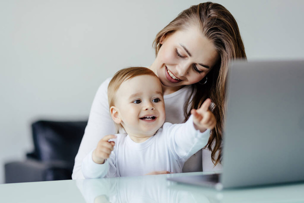 Νεαρή ανύπαντρη μητέρα μαμά με νεογέννητο βρέφος παιδί γιο χρησιμοποιώντας φορητό υπολογιστή, την αναζήτηση στο διαδίκτυο, βλέποντας κινούμενα σχέδια μαζί. - Φωτογραφία, εικόνα