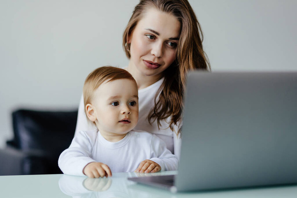 Молода мати-одиначка мама з новонародженим немовлям син використовує ноутбук, шукає в Інтернеті, дивиться мультфільми разом
. - Фото, зображення