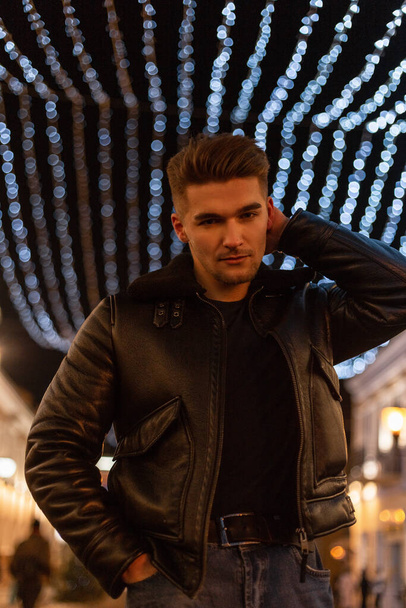 Stylish cool young business man model with hairstyle in fashionable black clothes with fashion leather jacket walking in the city with lights at night - Foto, immagini