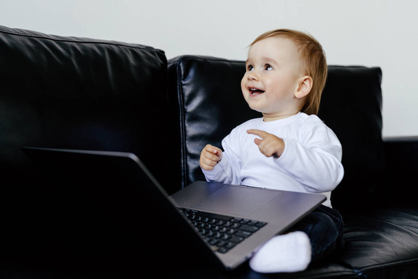 Picture of little cute boy using laptop computer while lies on sofa at home. Look at laptop. - Photo, Image