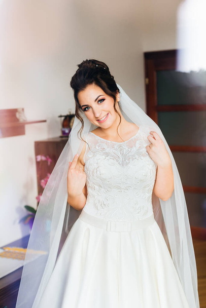 bride in white dress and bridal veil looks at the camera and smiles - Photo, Image