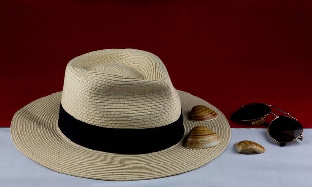 Panama şapkalı güneş gözlükleri ve deniz kabukları kırmızı ve beyaz bir tabanda. - Fotoğraf, Görsel