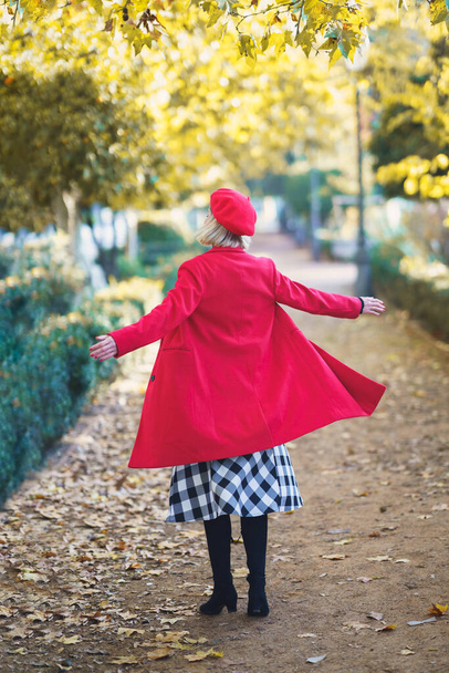 Full body back view of unrecognizable female in red outfit spinning on path with fallen leaves in park on autumn day - Photo, Image