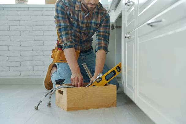 Close-up of confident handyman preparing tools to repair kitchen sink - Foto, imagen