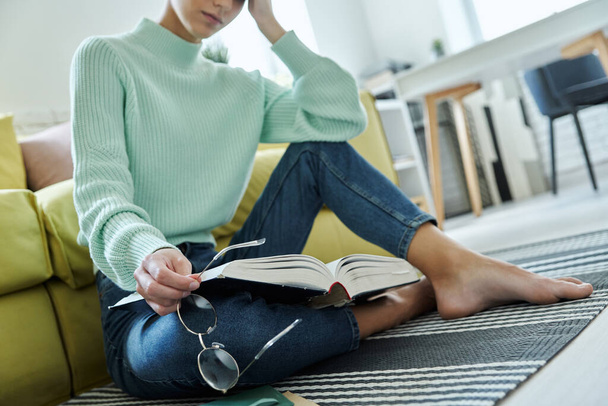 Close-up of tired woman holding book while sitting on the floor at home - 写真・画像