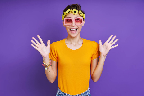 Excited funky woman with floral head wreath gesturing while standing against purple background - Фото, изображение