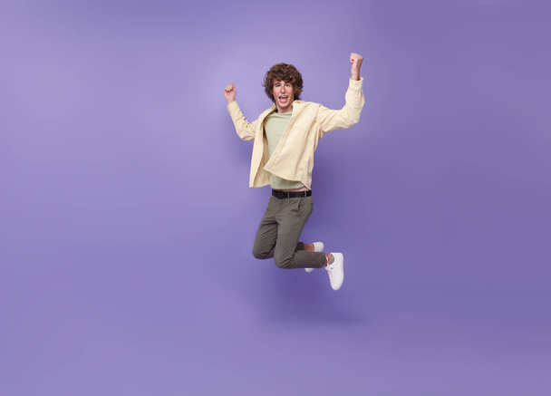 Cheerful guy jumping having fun rejoicing isolated on purple background - Photo, Image