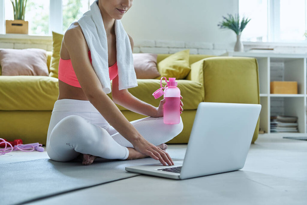 Close-up of young woman in sports clothing using laptop while sitting on exercise mat at home - Foto, immagini