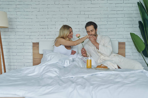 Handsome man kissing hand to his girlfriend while having breakfast in bed - Fotó, kép