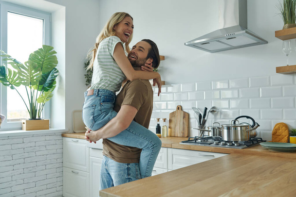 Beautiful young couple embracing and having fun at the domestic kitchen - Foto, imagen