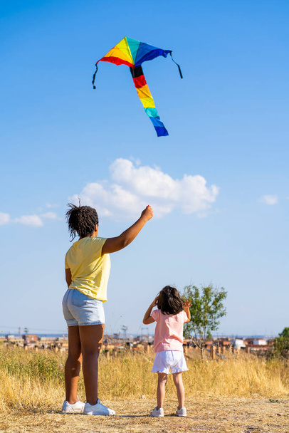 Mutter und Tochter fliegen einen bunten Drachen in der Natur  - Foto, Bild