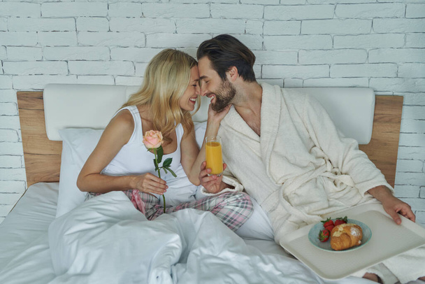 Young loving couple bonding while having breakfast in bed - 写真・画像