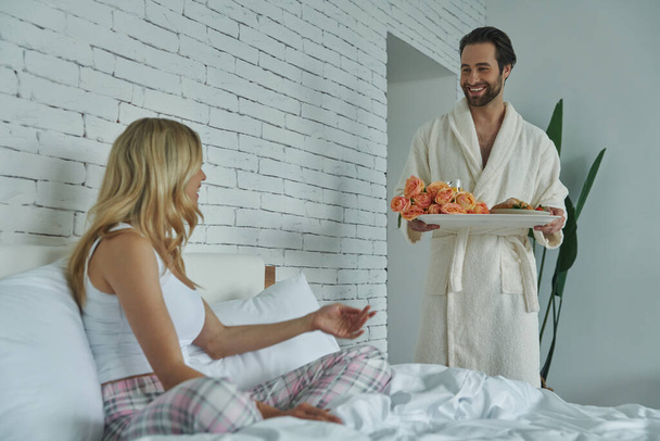 Young woman looking surprised while being served breakfast by her boyfriend in bed - Foto, immagini