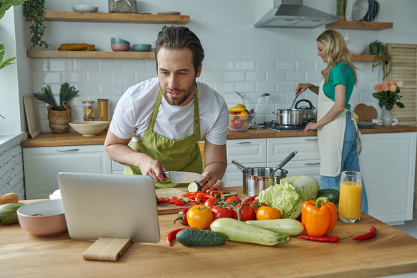 Handsome man using digital tablet while cooking together with his girlfriend at the kitchen - Foto, Bild
