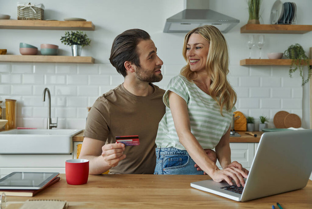 Beautiful young couple using credit card while shopping online from home - Foto, Bild
