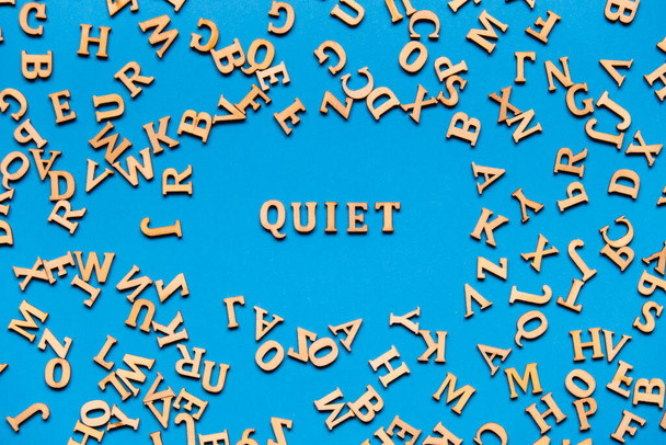 Λέξη QUIET κατασκευασμένο από ξύλινα γράμματα σε φωτεινό μπλε φόντο. Οι παρακινητικές λέξεις παραθέτουν την έννοια. Εμπνευσμένη φράση - Φωτογραφία, εικόνα