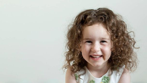 Portrét roztomilé pozitivní dívky s kudrnatými vlasy. Denní světlo. Bílé pozadí. Koncept dětí, dětství, vši, zdravé dítě. - Fotografie, Obrázek
