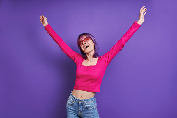 Happy young woman stretching out hands while standing against purple background - 写真・画像