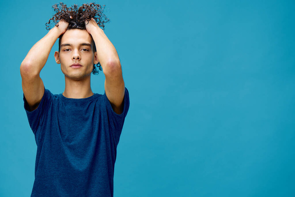 Handsome serious curly tanned Caucasian guy in basic t-shirt touches head posing isolated on over blue background. Lifestyle and Emotions concept. Good offer with copy space for ad - Fotografie, Obrázek