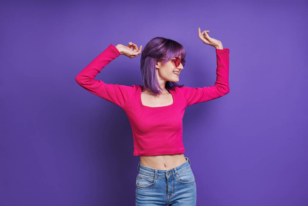 Cheerful young woman dancing while standing against purple background - Fotografie, Obrázek