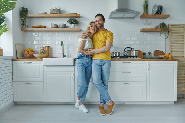Full length of young couple embracing while standing at the domestic kitchen - Photo, image