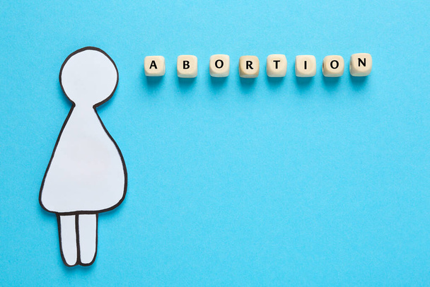 Word Abortion made of wooden cubes and pregnant woman paper cutout on light blue background, flat lay - 写真・画像