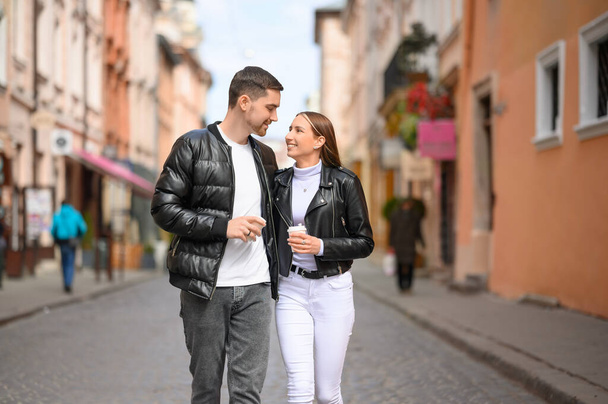 Lovely young couple with cups of coffee walking together on city street. Romantic date - Foto, imagen