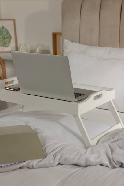 Modern dizüstü bilgisayarlı beyaz tepsi ve yatağın içinde akıllı telefon. - Fotoğraf, Görsel