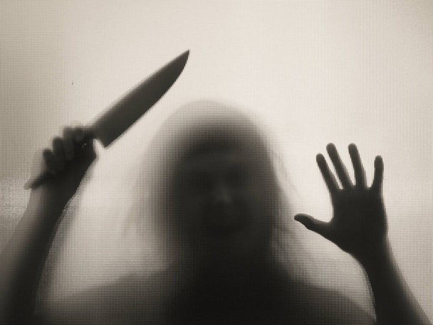Horror, halloween background - Shadowy figure behind glass holding a knife - Photo, image