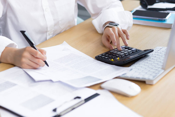 Close-up photo of a business womans hand on paper work, an accountant calculates and summarizes the results of the financial year with a calculator, an Asian woman works in the office. - Φωτογραφία, εικόνα