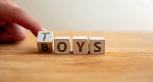 Toys for boys concept. Finger flips letter at wooden cube changing the word toys to boys. Advertisement at store, message for creative construction and learning from educational game. - 写真・画像