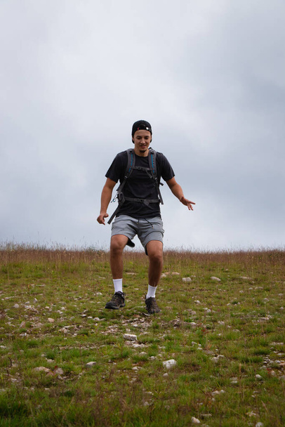 Swarthier Typ Mann läuft einen Schotterhügel hinunter und überprüft jeden seiner Schritte, um Verletzungen zu vermeiden. Aktive Sportler laufen über anspruchsvolles Gelände, um Fitness, Koordination und Bewegungsgenauigkeit zu verbessern. - Foto, Bild