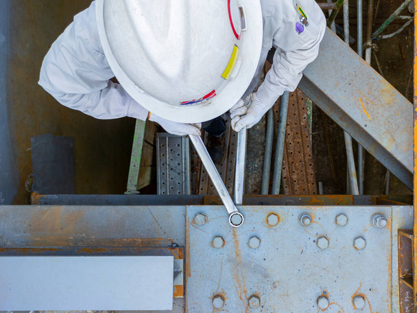 Arbeiter verwenden einen Schraubenschlüssel, um die Verbindungsplatte am Stahlträger der Stahlkonstruktion zu halten. - Foto, Bild