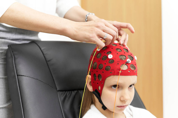 Przycięte zdjęcie lekarza łączącego elektrody z nakryciem głowy pacjenta do terapii biofeedback. - Zdjęcie, obraz