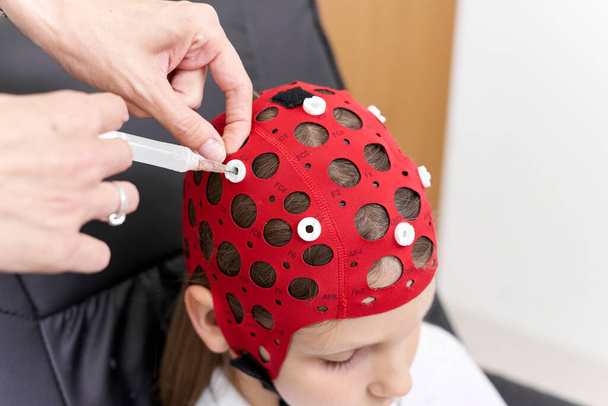 Visão superior da mão de um médico aplicando um líquido em um capacete de pacientes para terapia de biofeedback. - Foto, Imagem