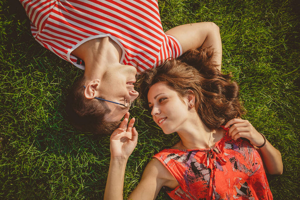 Joven pareja amorosa acostados juntos cabeza a cabeza en una hierba en verano. Un picnic familiar. Ambos vestidos de rojo y tomados de la mano. Vista superior. - Foto, imagen