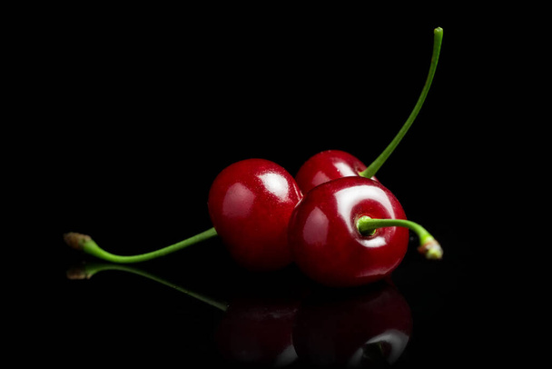 Red cherry berries on a black background with mirror. Three cherries. - 写真・画像