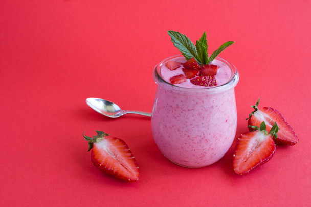 Přírodní jogurt s jahodami ve skleněné nádobě na červeném pozadí. Detailní záběr. Kopírovat prostor. - Fotografie, Obrázek