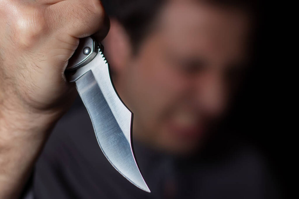 Knife in the hand of a man. Threat with knife. Man attack with knife. Crime, violence. Selective focus. Blurred face - Photo, Image